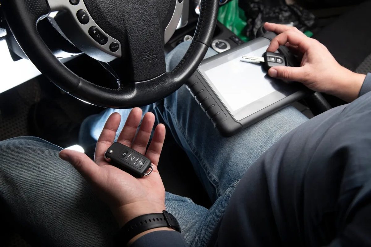 Technician programming a key fob with a diagnostic tablet inside a vehicle